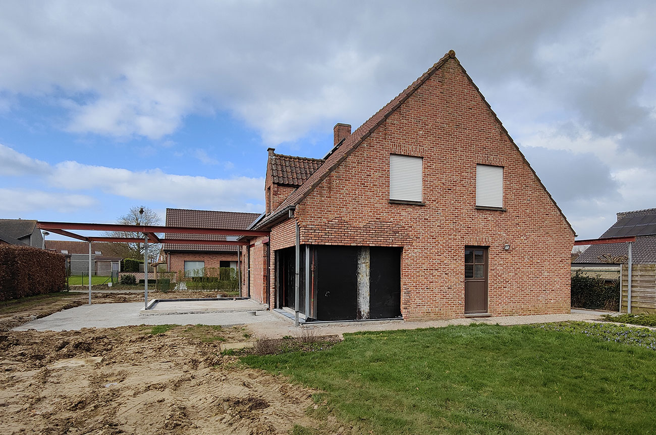 Zicht op een nieuwe aanbouw bij een bestaand huis. De aanbouw wordt gedragen door metalen balken.