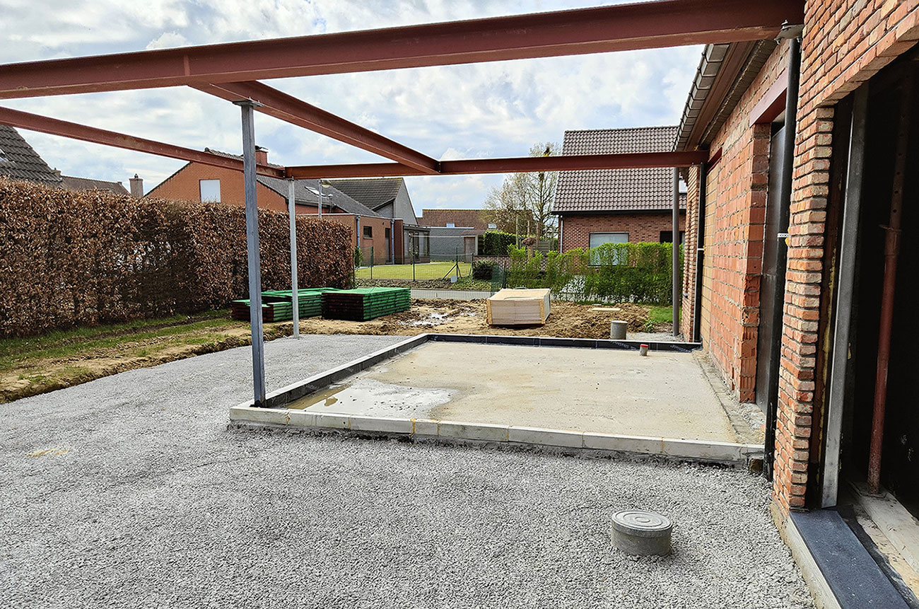 Zicht op een nieuwe aanbouw bij een bestaand huis. De aanbouw wordt gedragen door metalen balken.